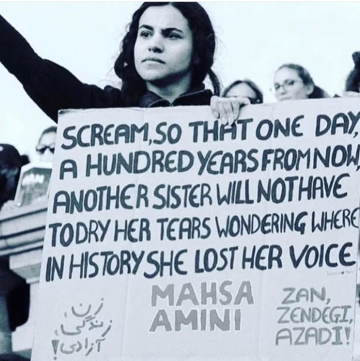 a woman holding up a sign with words written on it in front of other people