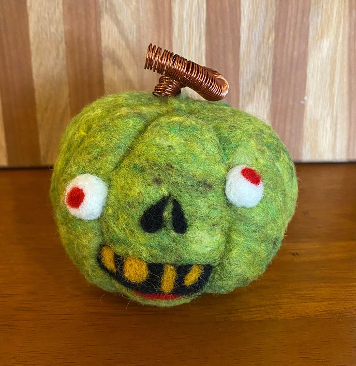 a green stuffed pumpkin with red eyes on a wooden table