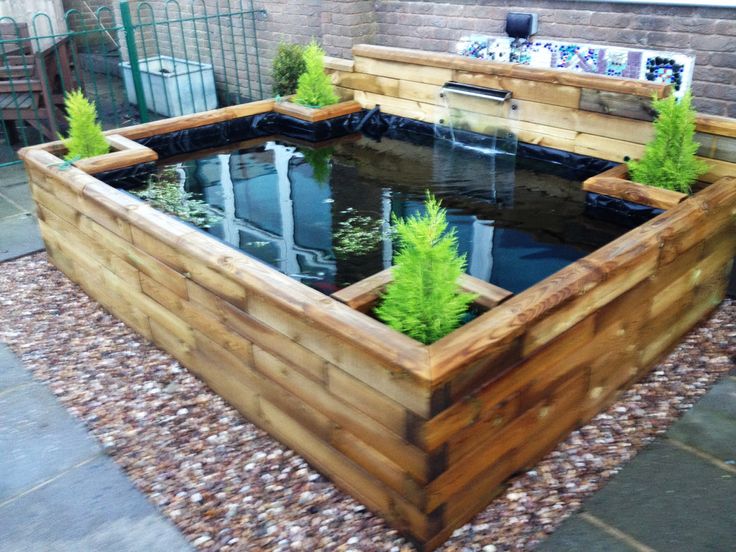 a fish pond in the middle of a garden with gravel around it and trees growing inside