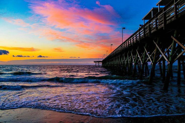 a pier that is next to the ocean with waves coming up on it at sunset