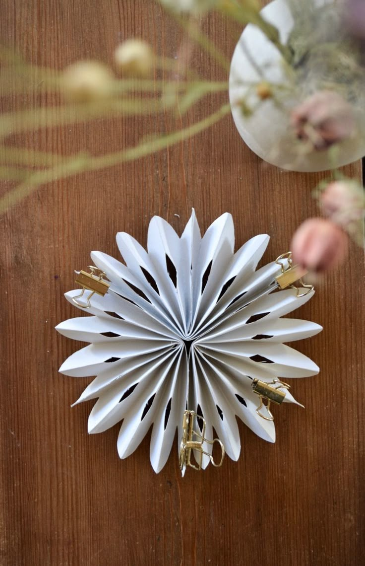 an origami flower on a wooden surface with flowers in the background and gold scissors stuck to it