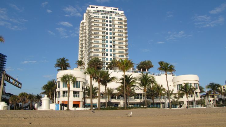 a tall white building sitting on top of a beach next to palm trees and a blue sky