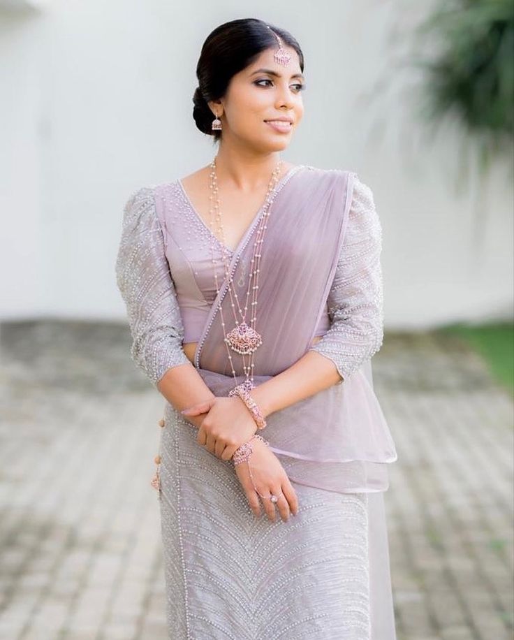 a woman wearing a dress and necklace standing in front of a white wall with her hand on her hip