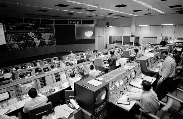 an old control room with many monitors and people working on the computers in it's desks