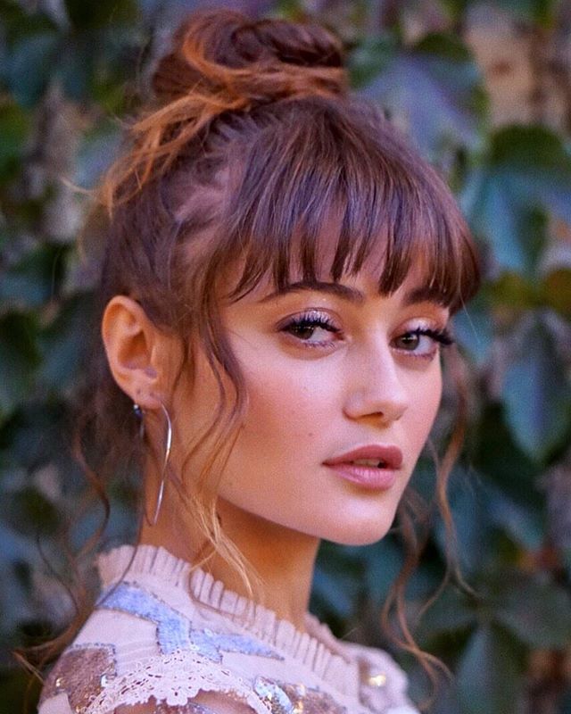 a close up of a person wearing a dress and hair in a bun with bangs