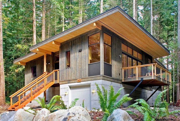 a house in the woods surrounded by rocks and trees with stairs leading up to it