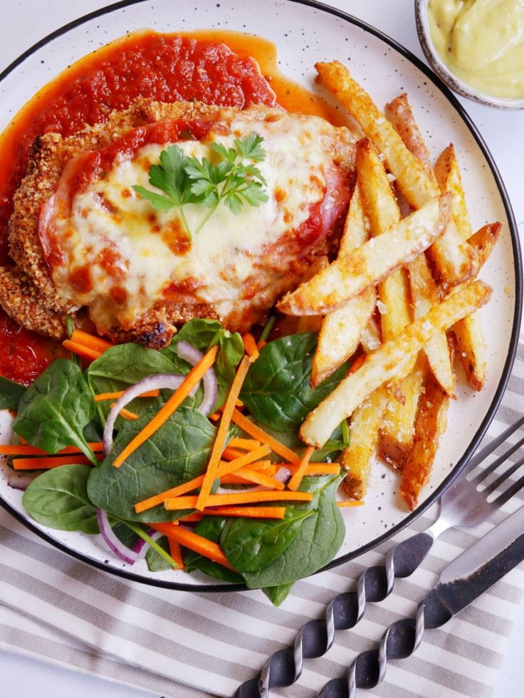 a white plate topped with meat covered in sauce next to french fries and veggies