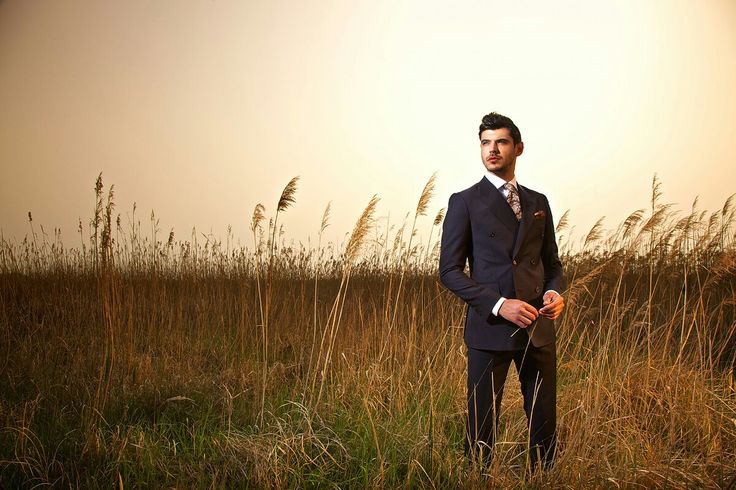 a man in a suit standing in the middle of tall grass with his hands in his pockets