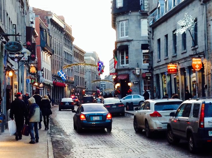 people are walking down the street in an old city with cars parked on both sides