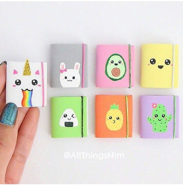 a hand is holding several small notebooks with different designs on them, including an unicorn, cactus, and other animals