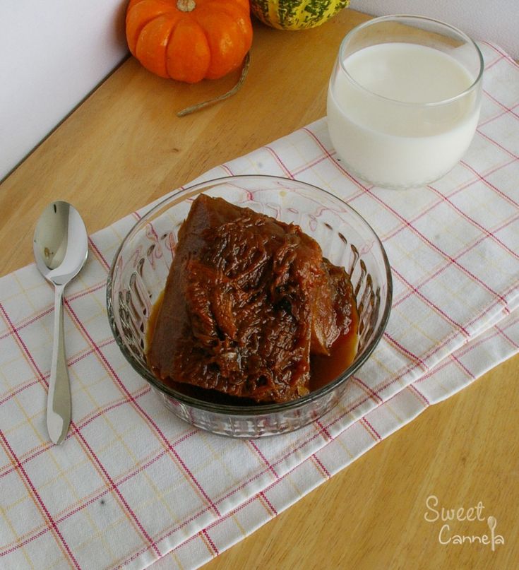 a glass bowl filled with meat and sauce next to a cup of milk on a table