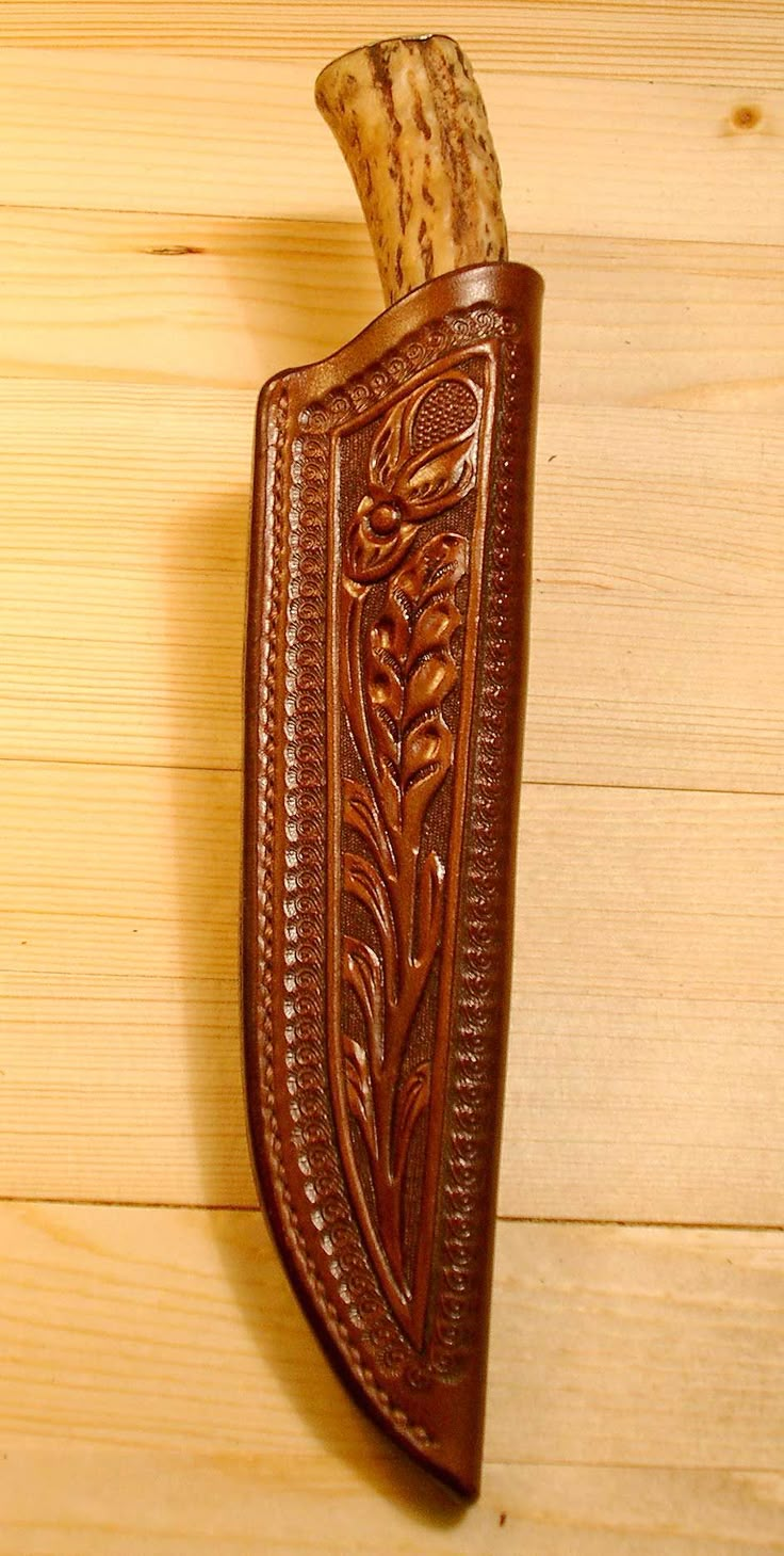 a leather sheath with an intricate design on the outside and inside, hanging from a wooden wall