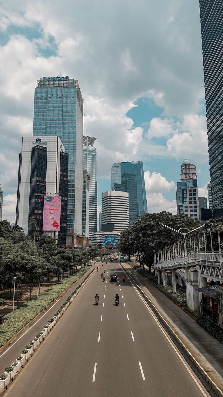 an empty city street with tall buildings in the back ground and cars driving down it