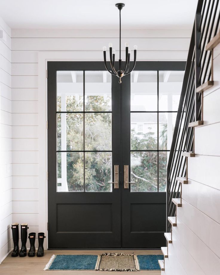 an entryway with black doors and rugs on the floor, chandelier hanging from the ceiling