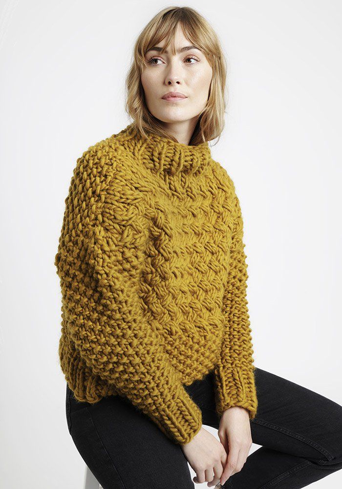 a woman is sitting on a stool wearing a yellow knitted sweater and ...