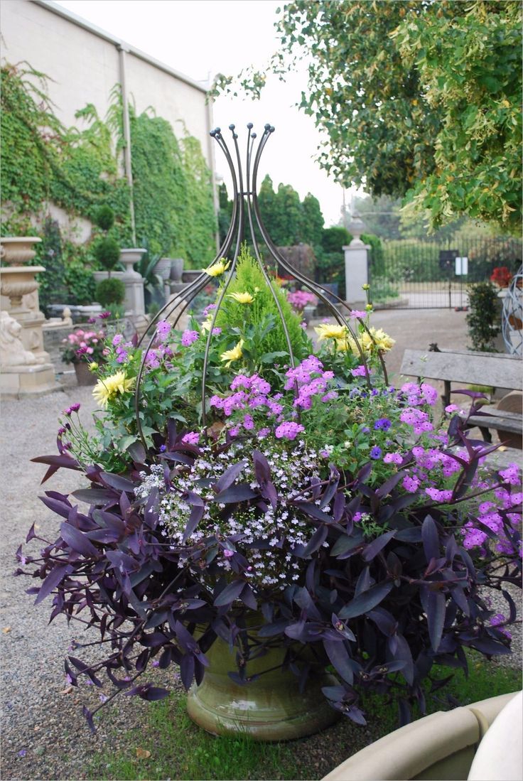 purple and yellow flowers are in a green vase on the ground near a park bench