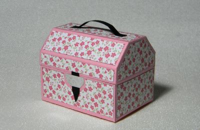 a small pink and white box with floral designs on it sitting on a plain surface