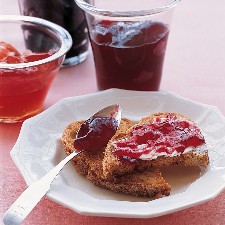 two pieces of toast with jam and jelly on them sitting on a plate next to cups