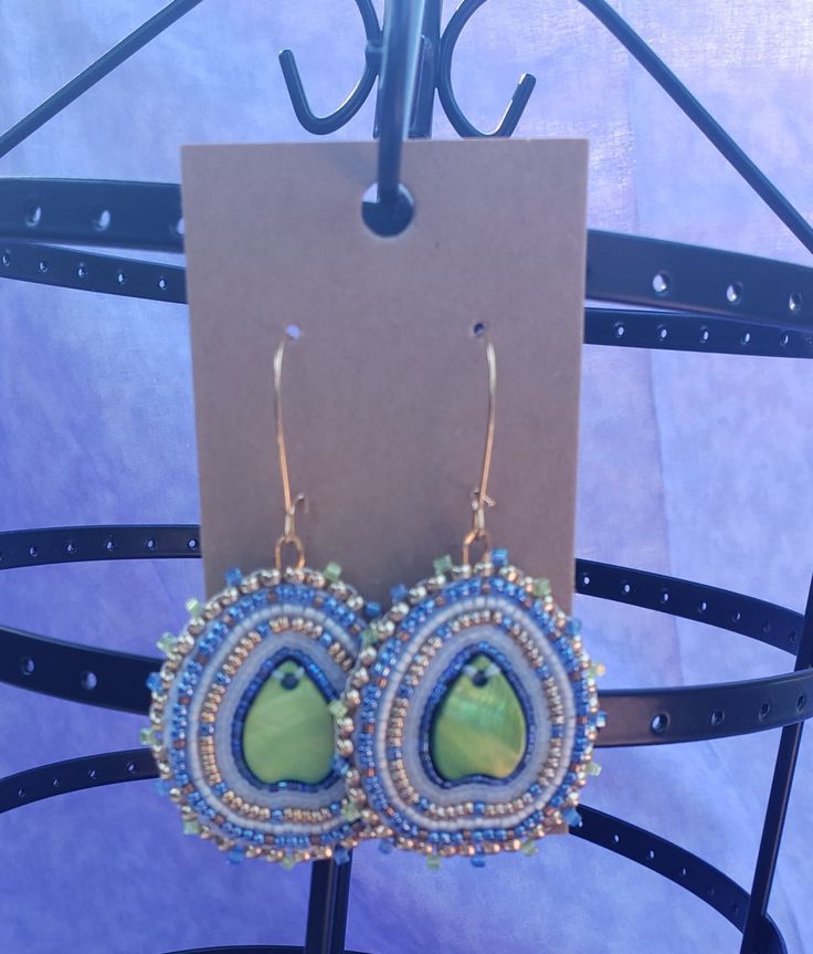 Green shell center with clear, blue, and gold beads. Another very simple design that looks amazing and complex with the addition of the gold beads and the shape of the shell. The slightly inward curve of the shell also adds to that, making it so much more then what you see. Bohemian Embellished Beaded Earrings, Blue Beaded Teardrop Jewelry, Blue Teardrop Beaded Jewelry, Blue Teardrop Beaded Earrings For Festival, Artisan Blue Jewelry With Bead Caps, Bohemian Adjustable Embellished Jewelry, Teardrop Beaded Jewelry For The Beach, Beaded Teardrop Jewelry For The Beach, Artisan Blue Beaded Earrings With Tiny Beads