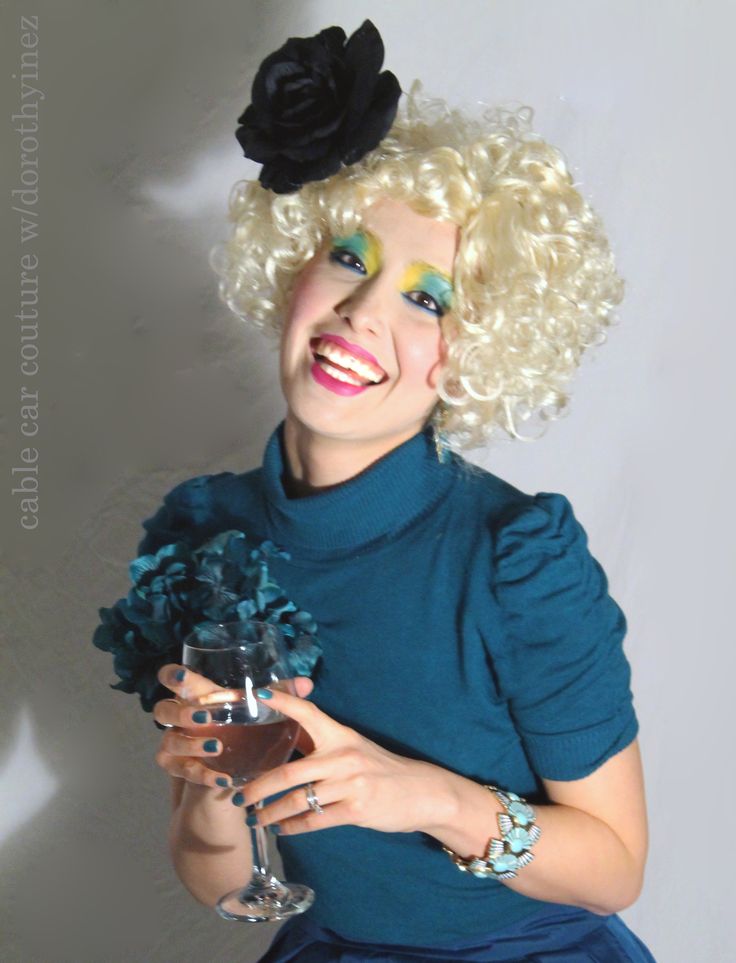 a woman with blonde hair holding a wine glass and flower in her hand while wearing a blue dress