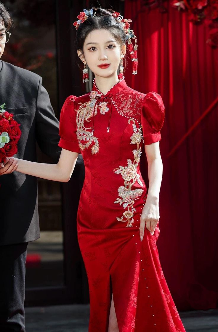 The dress adorned with a stunning phoenix print, adding an elegant, heritage-inspired aesthetic. The phoenix motif symbolizes prosperity and good fortune, making this gown a wonderful choice for special occasions. Whether you're looking for a showstopping wedding dress or a special event outfit, this red qipao offers the perfect fusion of time-honored Chinese craftsmanship and modern stylistic flair. Pair it with delicate accessories to create a refined look, or amp up the glamour with bold jewe Traditional Red Cheongsam For Wedding, Traditional Red Wedding Cheongsam, Red Brocade Wedding Dress, Elegant Red Ceremonial Dress, Traditional Short Sleeve Cheongsam For Wedding, Elegant Dresses For Ceremonies And Festivals, Elegant Dresses For Ceremony And Festivals, Red Dress For Wedding And New Year, Red Dress For Wedding And New Year's Eve