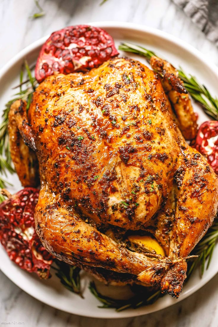 a roasted chicken on a white plate with cranberries and rosemary garnish