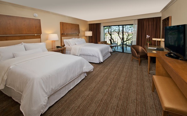 a hotel room with two beds and a flat screen tv on the wall, in front of a sliding glass door