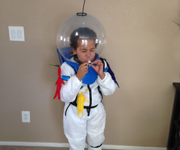 a young boy dressed up as an astronaut holding a blue object in his hand while standing on the floor