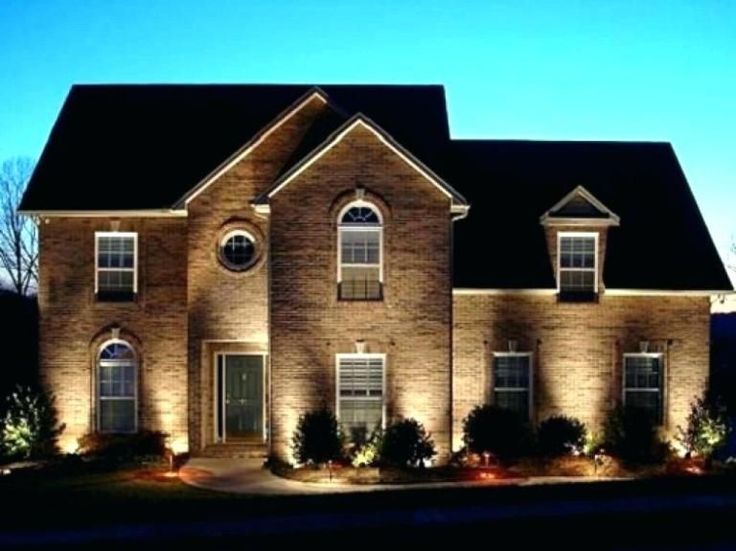 a large brick house with lights on it's windows and bushes in the front yard