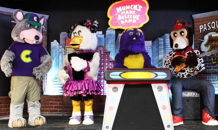 three people in animal costumes sitting on stools next to an arcade game machine and another person standing behind them