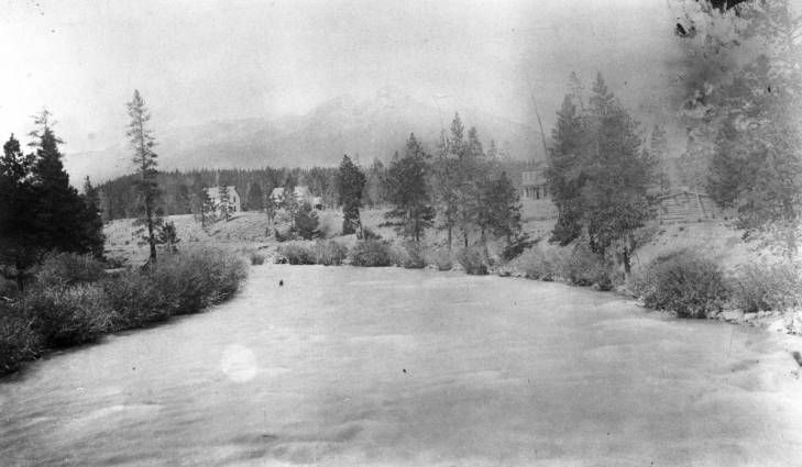 an old black and white photo of a river with trees in the background on a cloudy day