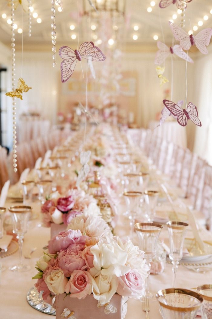 a long table is set with pink flowers and butterflies hanging from it's ceiling