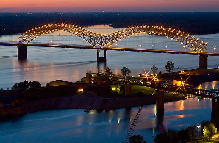 the bridge is lit up at night with lights on it's sides and reflecting in the water