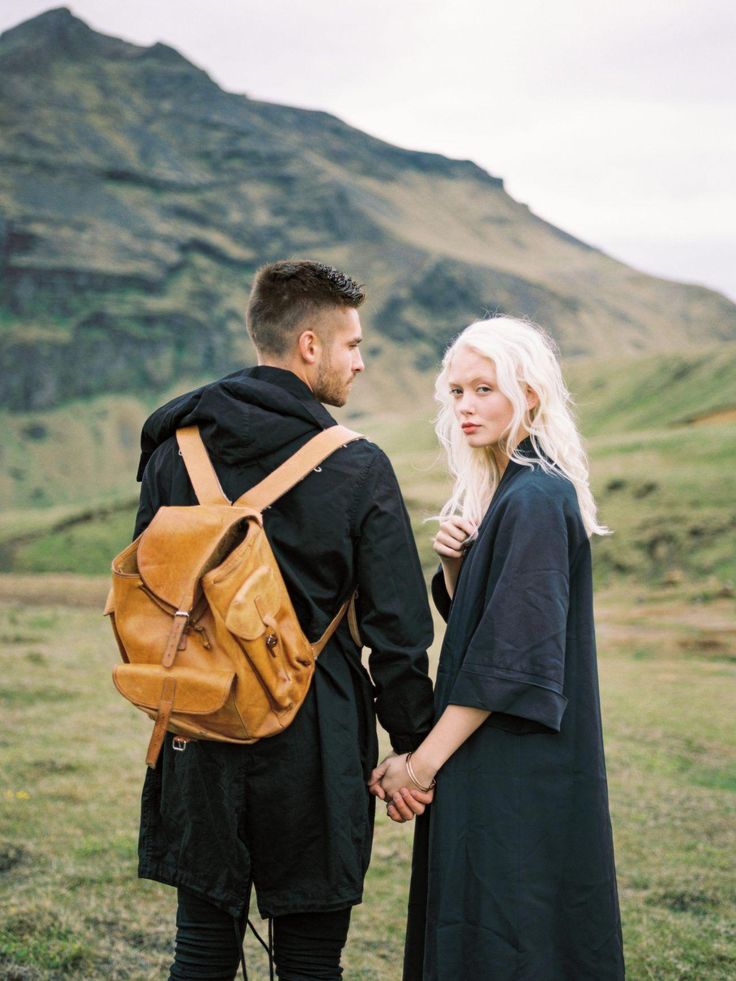 a man and woman standing next to each other with a backpack on their back, looking at each other