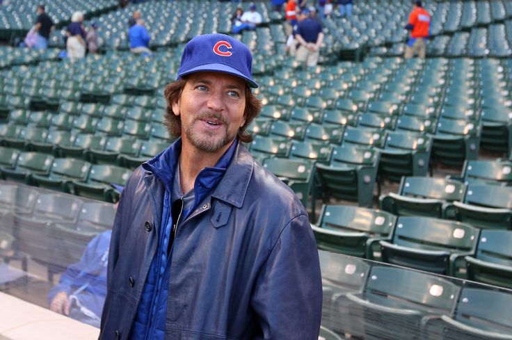 a man wearing a chicago cubs hat standing in the bleachers at a baseball game