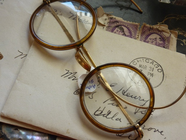 a pair of glasses sitting on top of an old envelope with stamps in the background