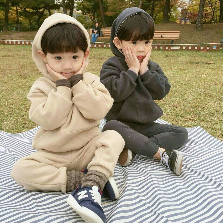 two young children sitting on top of a blue and white blanket next to each other