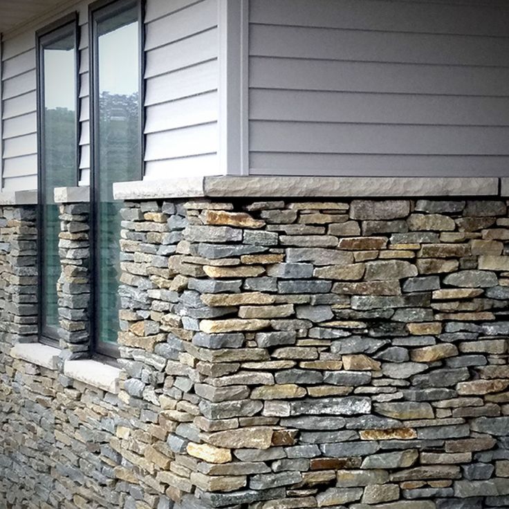 a cat sitting on top of a stone wall next to a window sill in front of a house