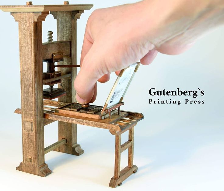 a hand is holding a piece of wood with a machine on it and the words guttenberg's printing press