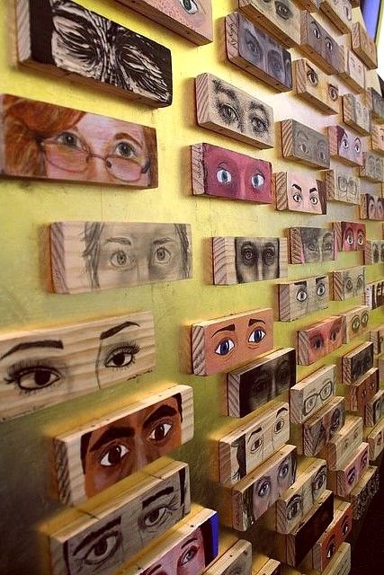 a woman standing in front of a wall covered with wooden boxes and eyeballs on them