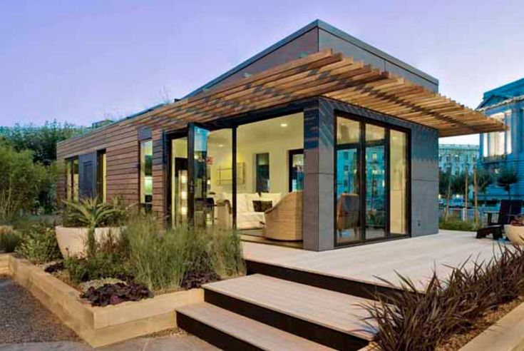 a modern home with wooden steps and plants in the front yard, surrounded by greenery