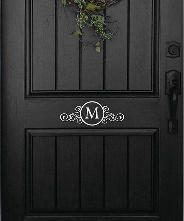 a black front door with a wreath and monogrammed letters on the bottom panel