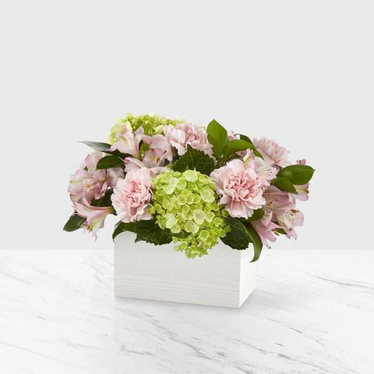 a white vase filled with pink and green flowers on top of a marble countertop