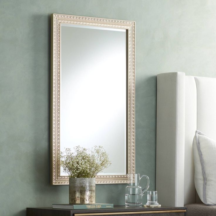 a mirror sitting on top of a dresser next to a vase with flowers in it