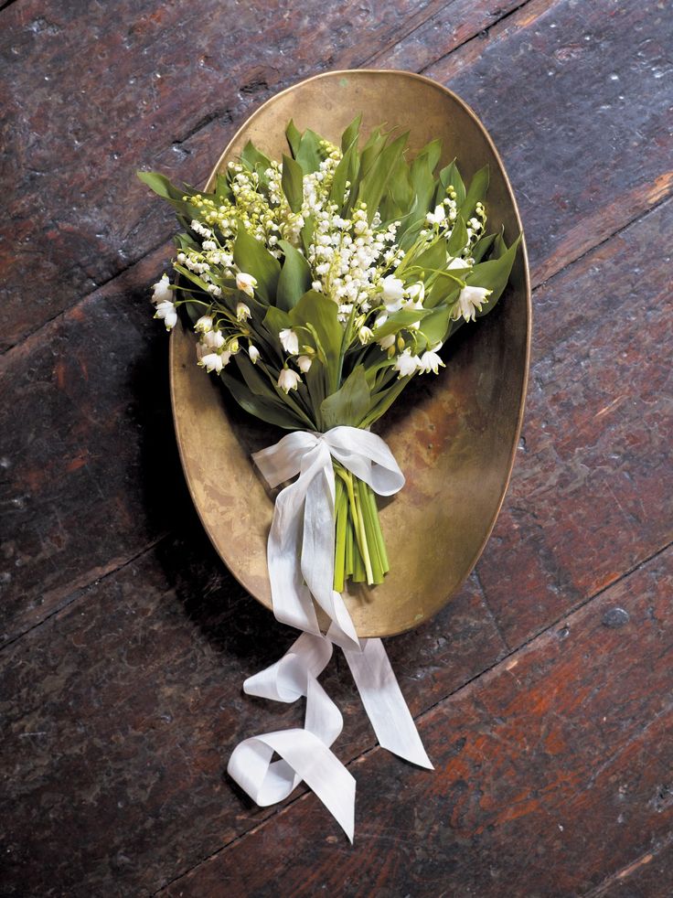 a bouquet of flowers on a plate with white ribbon tied around the edge, sitting on a wooden table