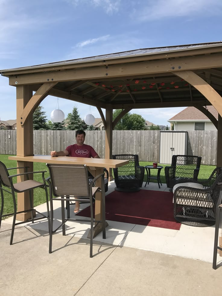 a man sitting at a table under a wooden gazebo with chairs and tables around it