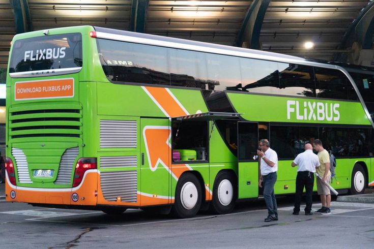 people are standing in front of a green and orange bus