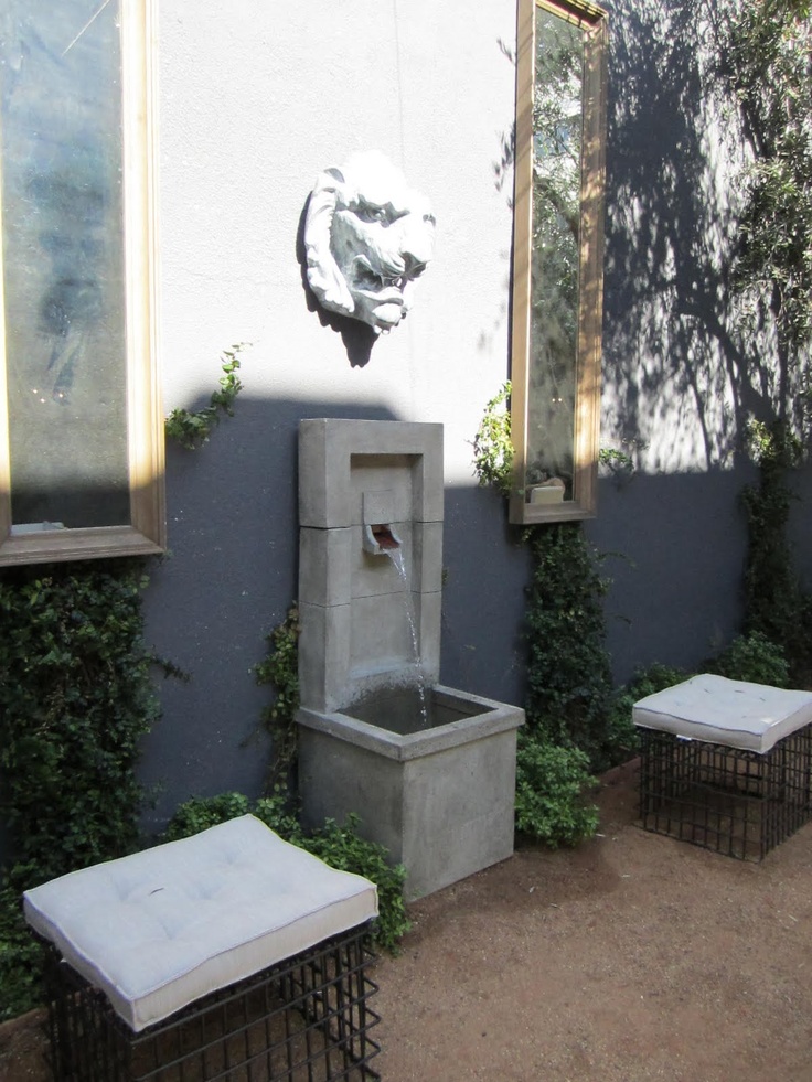 an outdoor fountain and benches in front of a building with ivy growing on the walls