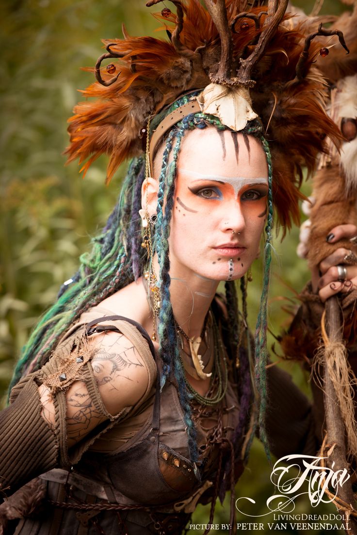 a woman with dreadlocks and feathers on her head is standing in the woods