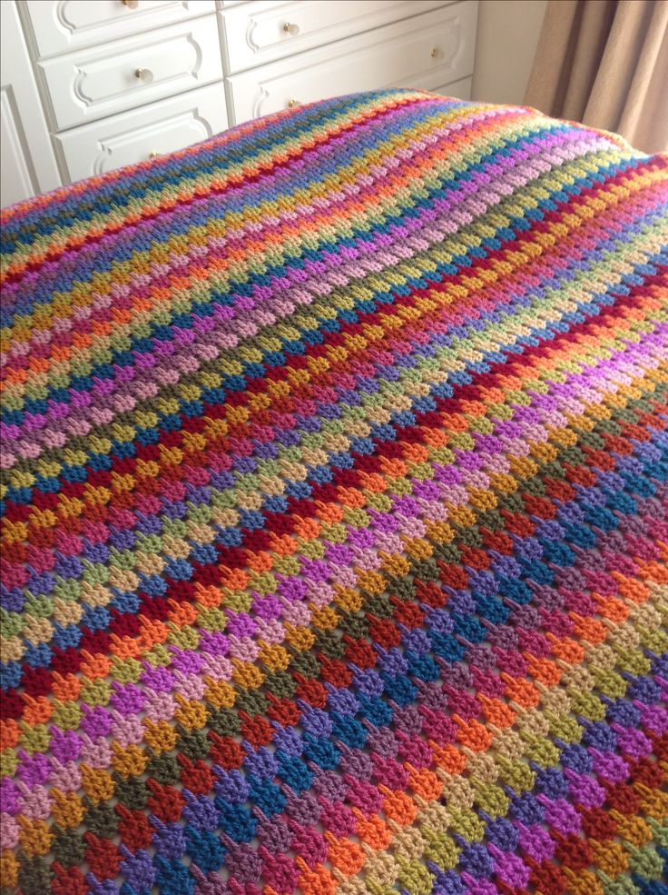 a multicolored crocheted blanket sitting on top of a bed next to a white dresser